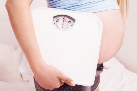 A pregnant woman holds a scale: weight loss is one of the harbingers of childbirth.